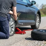 Un mécanicien utilisant une clé en croix pour desserrer les écrous d'une roue de voiture soulevée par un cric.