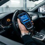 Une main tient un scanner OBDII affichant le code défaut P0420 à l'intérieur d'un véhicule avec le voyant moteur allumé.