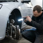Un mécanicien inspecte la suspension d'une voiture sur un pont élévateur avec une lampe torche LED.