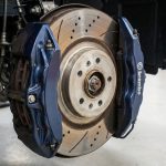 Gros plan sur un disque de frein perforé avec un étrier bleu Brembo dans un atelier automobile.