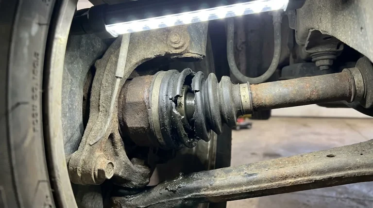 Un soufflet de cardan de voiture gravement fissuré et usé, exposé sous une lumière LED.