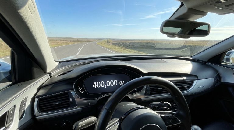 Vue du poste de pilotage d'une voiture sur une route affichant 400 000 km au compteur numérique.