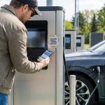 Un homme scanne un QR code suspect sur une borne de recharge de voiture électrique avec son smartphone.