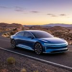 Une berline électrique bleue Lucid Air circulant sur une route sinueuse dans un paysage désertique au coucher du soleil.