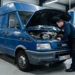 Un mécanicien examine le moteur d'un fourgon bleu Iveco Daily dans un garage automobile bien éclairé.